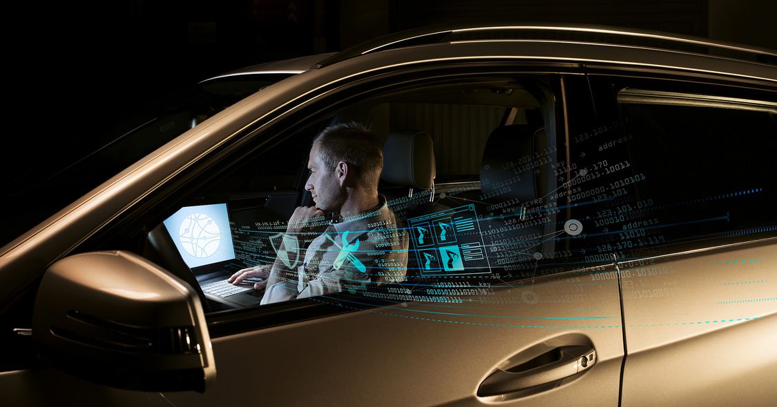 Ein Mann sitzt nachts in einem parkenden Auto und greift aus der Ferne auf eine Fabrik mit seinem Laptop zu, aus dem stilisierte Daten strömen 