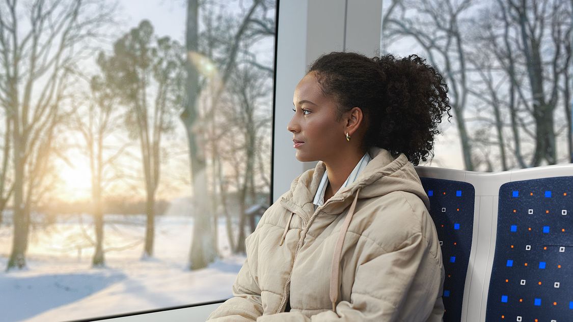 Eine junge Frau fährt in einer Siemens Mobility Inspiro Metro durch eine winterlicher Landschaft in Oslo.