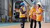 Drei Vertreter der Allianz für Verfügbarkeit, die Sicherheitswesten und Helme tragen, tauschen vor einem Zug im Bahndepo Informationen aus