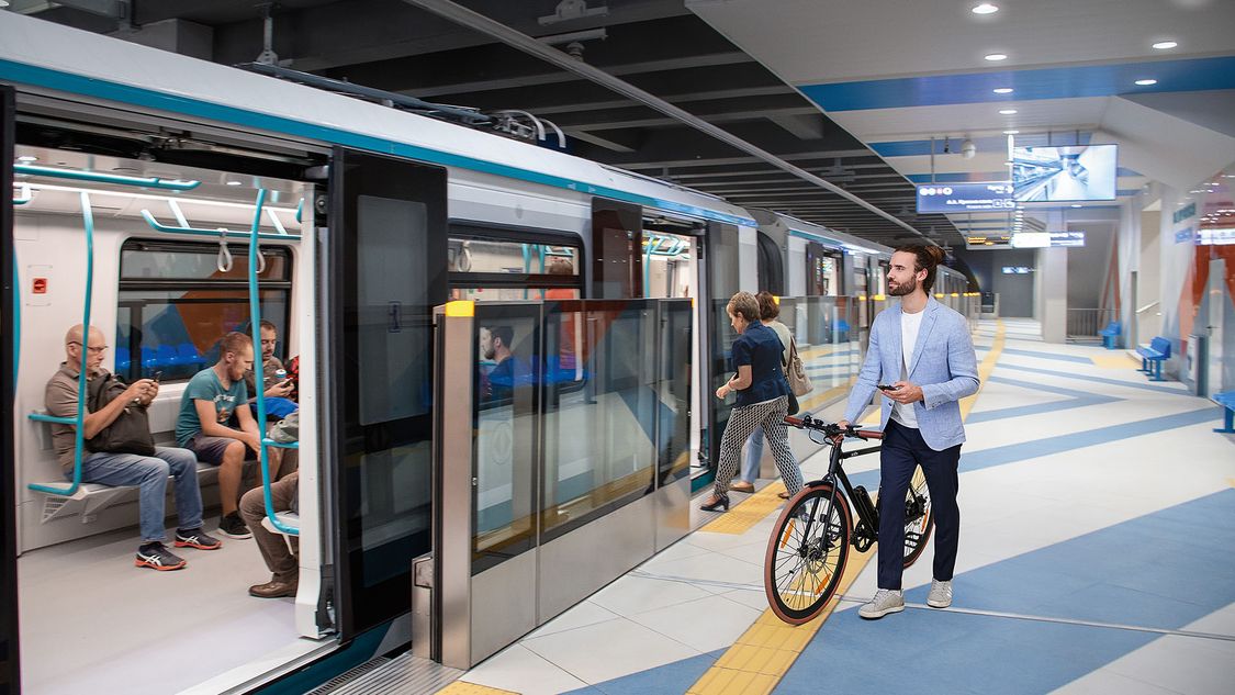 Ein Mann geht mit seinem Fahrrad an einem Bahnsteig in Sofia entlang und macht sich zum Einsteigen in die Siemens Mobility Inspiro Metro bereit.