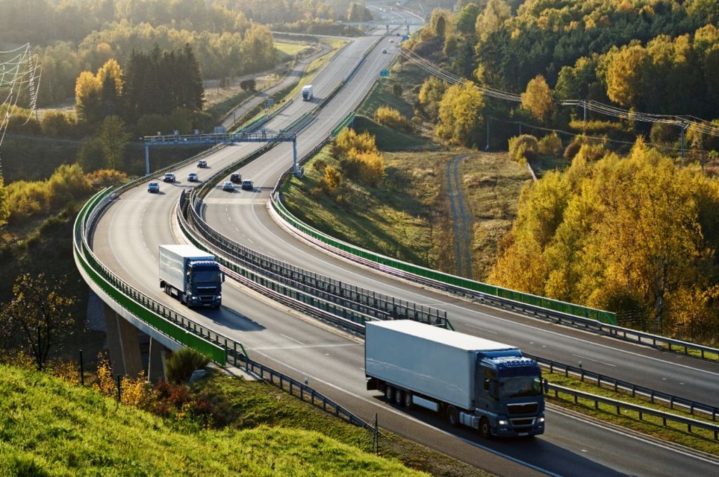 Trucks driving on highway with electronic toll gates, in autumn