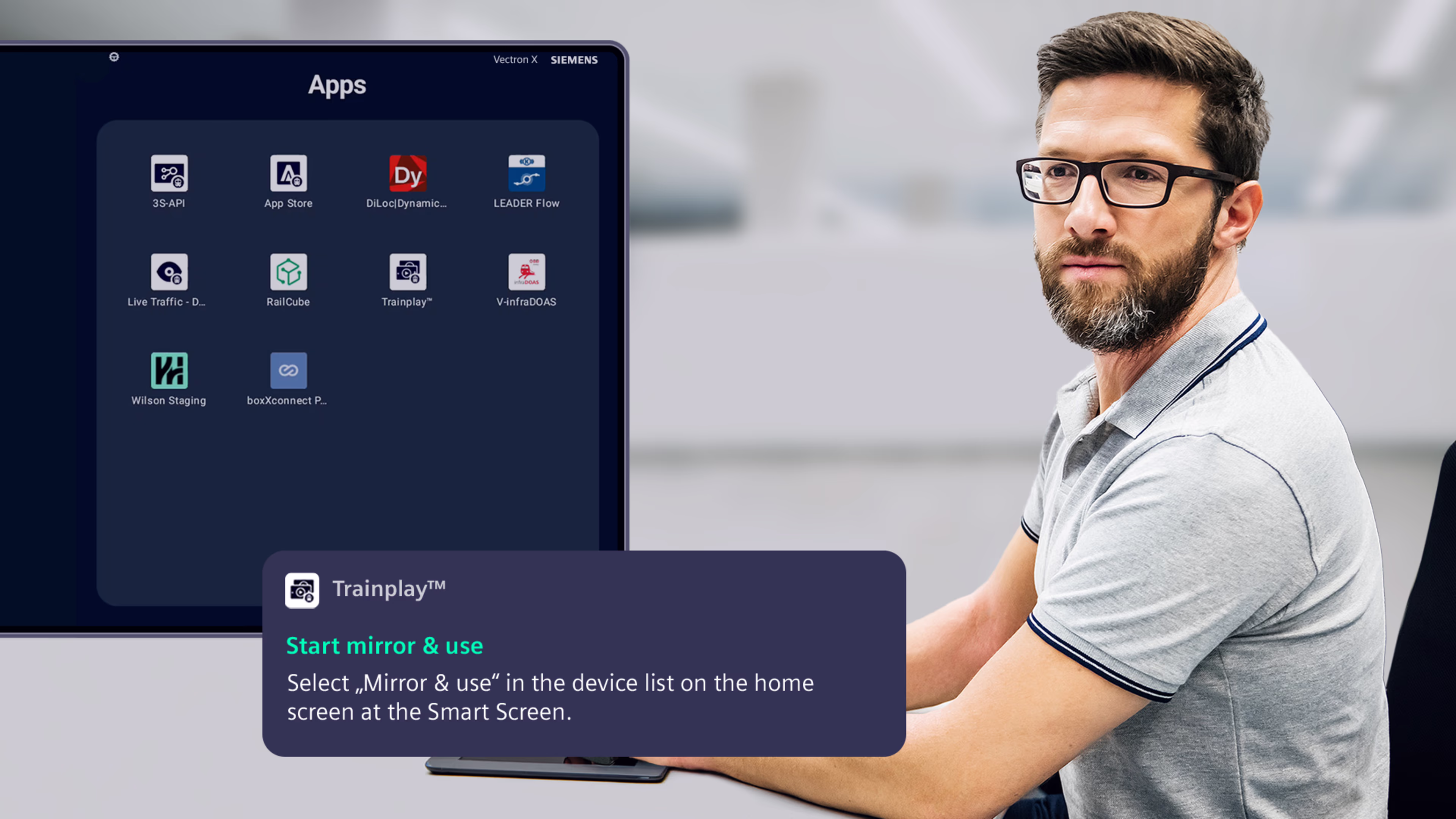 Ein Mann sitzt an einem Schreibtisch und schaut in Richtung von Screenshots aus einer App. Siemens Mobility Vectron X Produkt Bundle Driver Experience