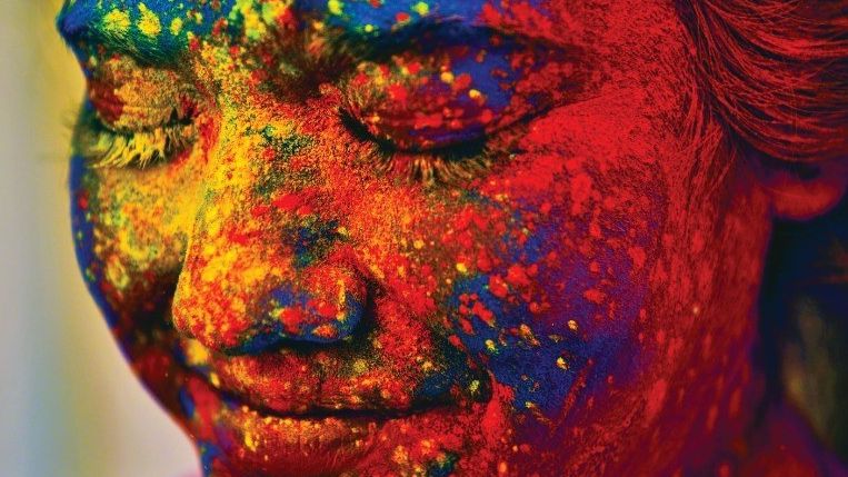 Girl with closed eyes. The face is splashed in paint in blue, red, yellow and green