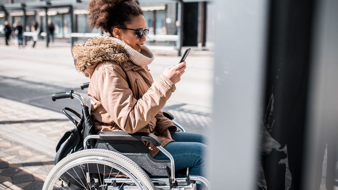 A female passenger in a wheelchair enjoys an improved passenger experience thanks to intermodal travel apps which tell her exactly where she needs to go while navigating multimodal mobility systems 