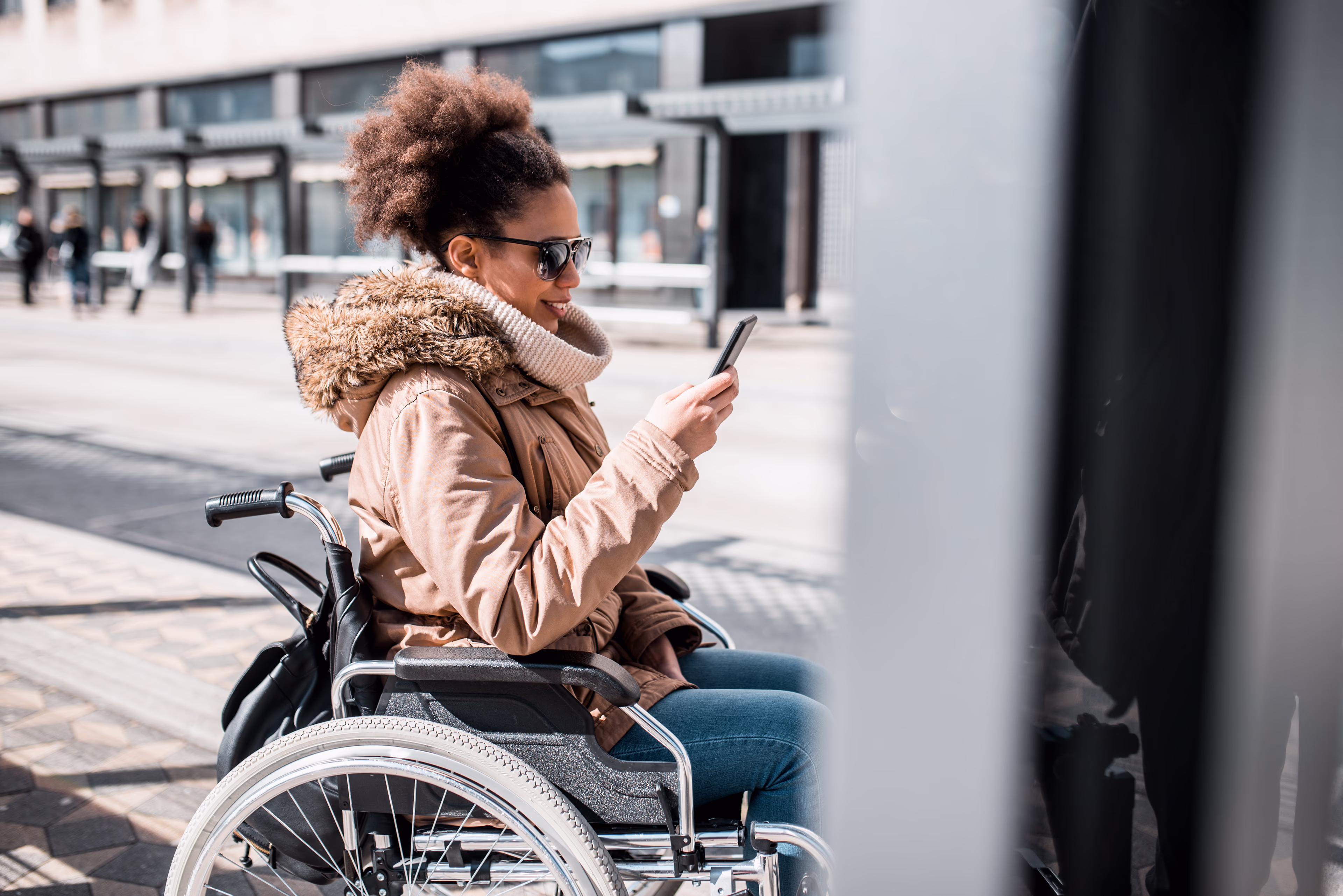 Rollstuhlfahrerin blickt am Bahnsteig auf ihr Smartphone