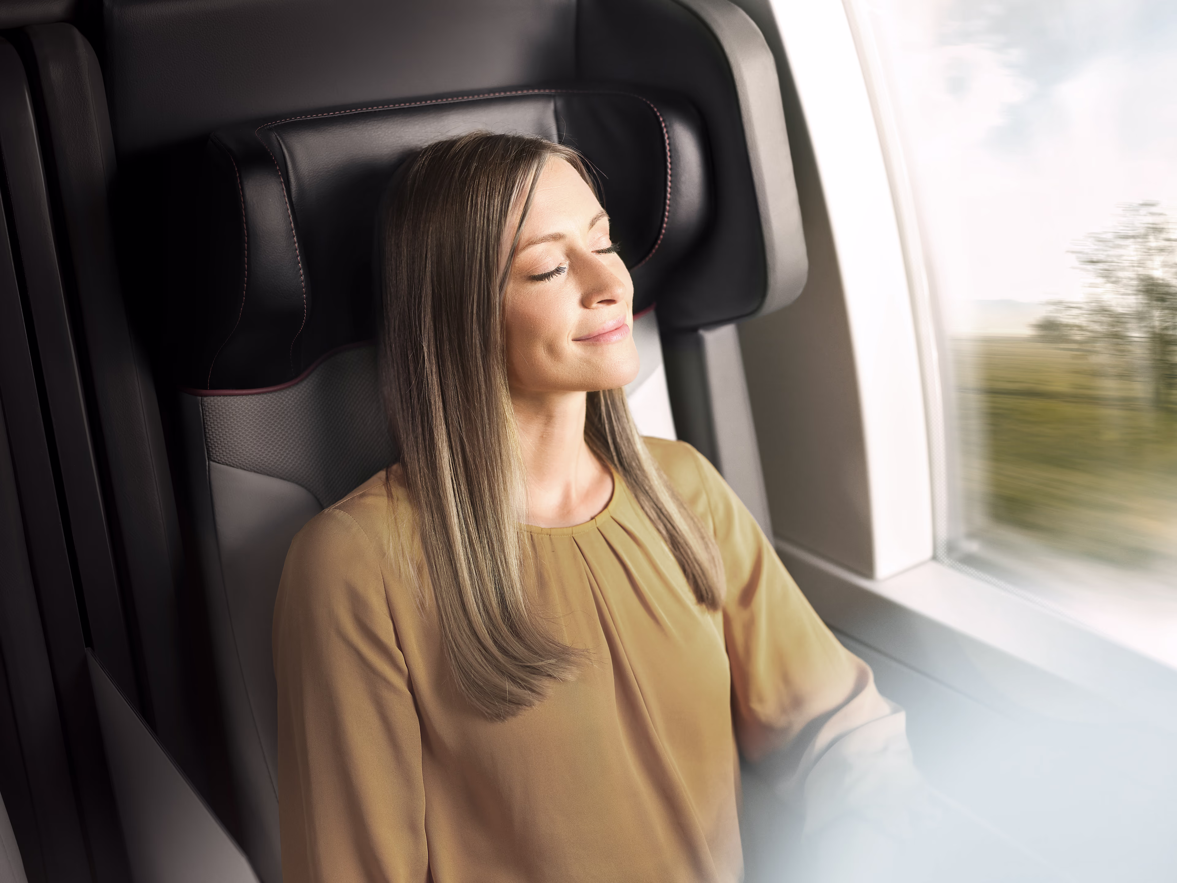 Eine Frau sitzt sehr entspannt in einem Zugabteil und hat die Augen geschlossen. Fahrgastinformation Plus