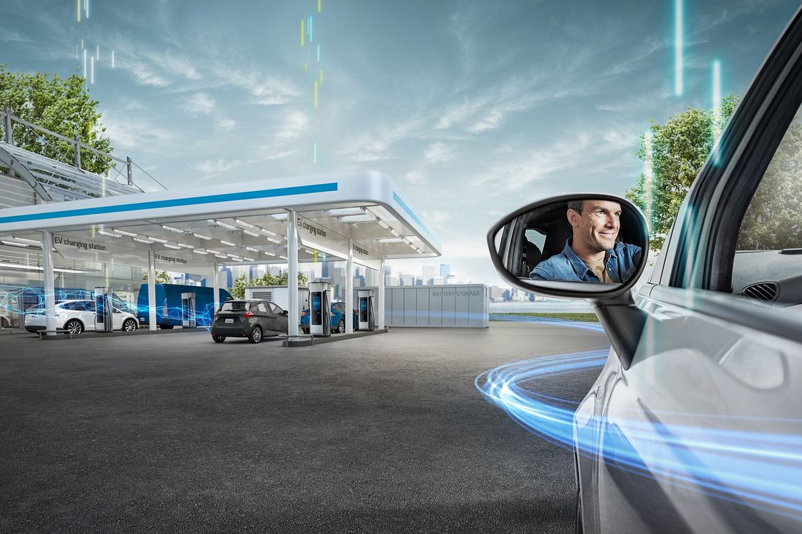 An EV approaches a state-of-the-art charging station. We see the driver in the side mirror.