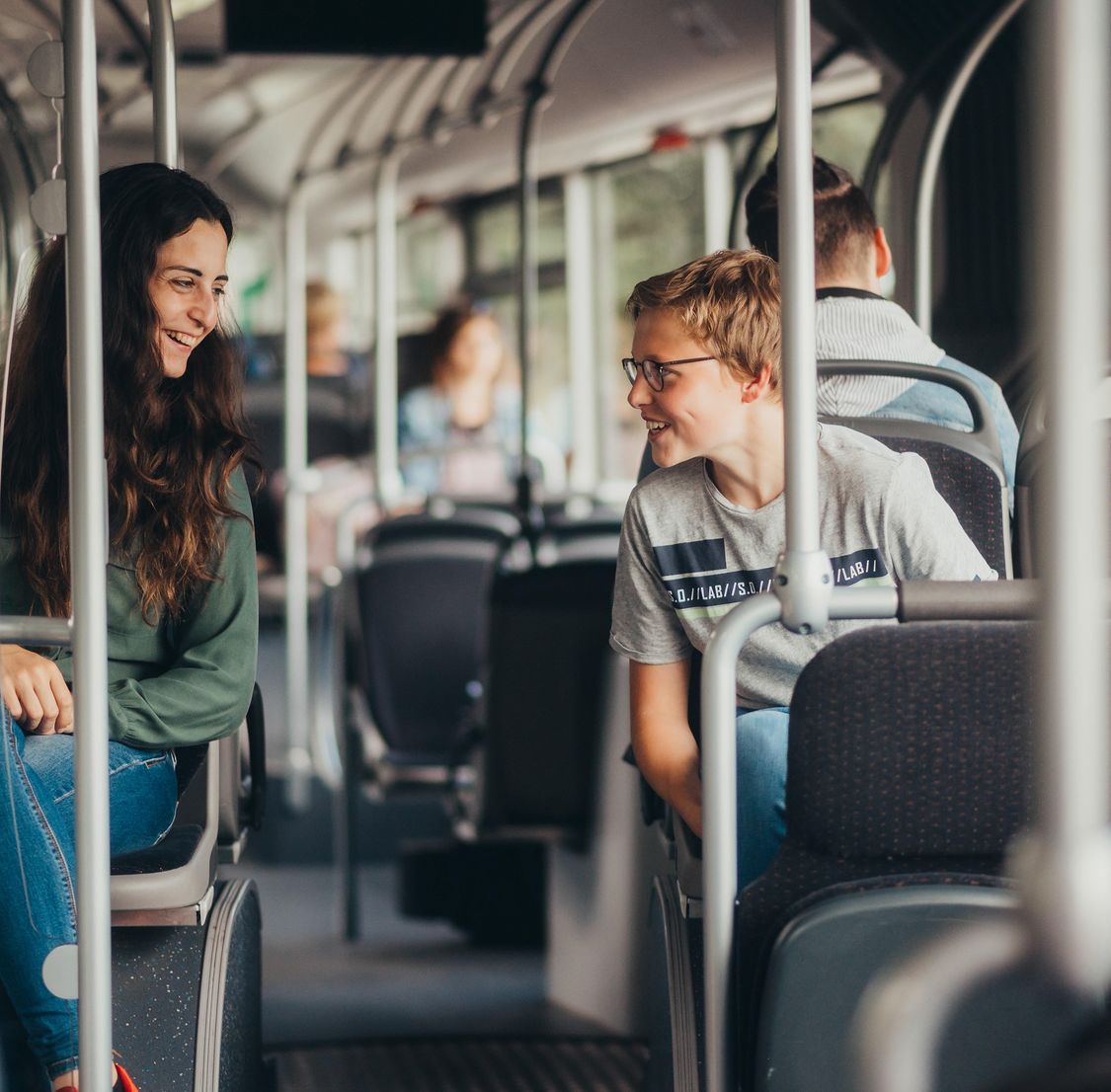 a girl and a boy are riding on a bus an smiling at each other