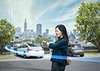 Person mit Smartwatch vor parkenden Elektroautos und der Skyline von San Francisco