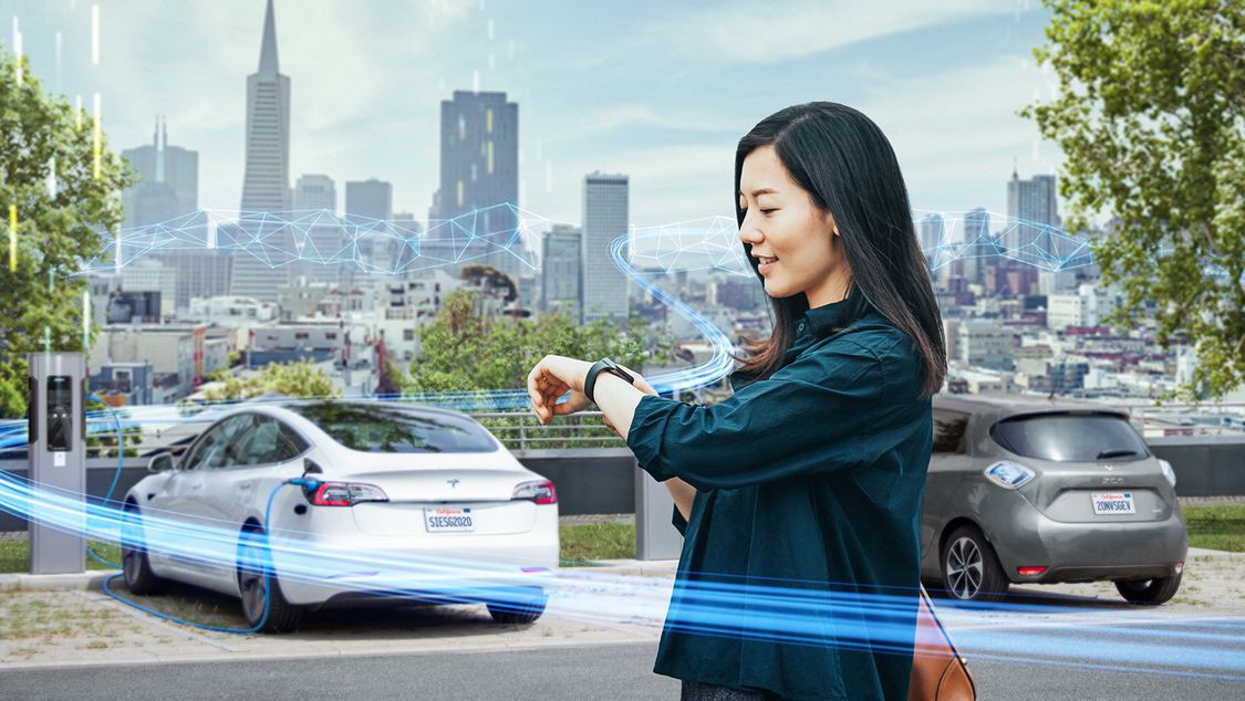 Smart infrastructure grid edge image with woman looking at her watch next to an electric car charging station