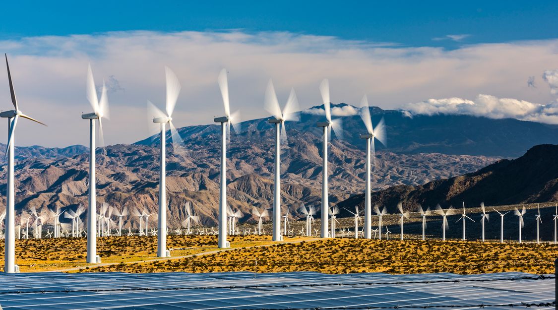 wind turbines and solar panels on a field in front of mountains