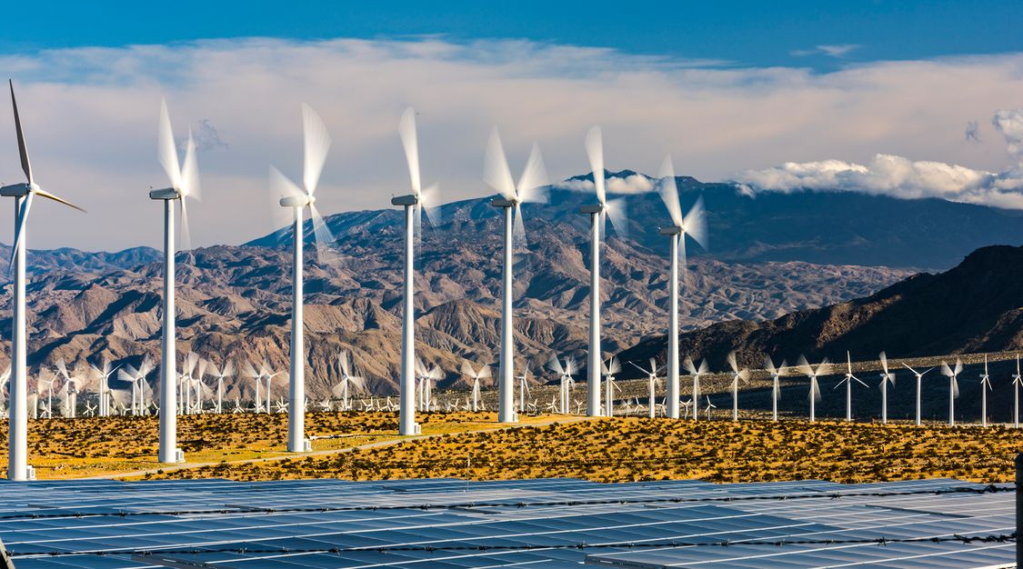 wind turbines and solar panels on a field in front of mountains