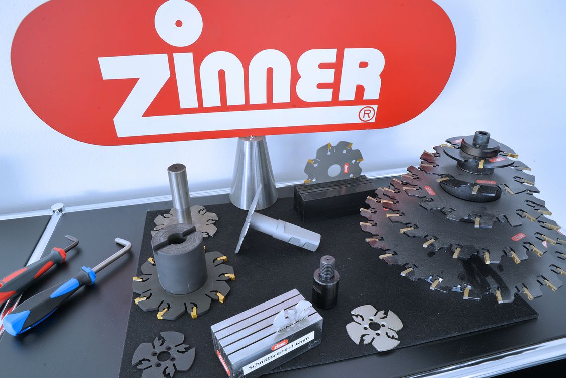 Photo of various workpieces in front of the red and white Zinner company logo