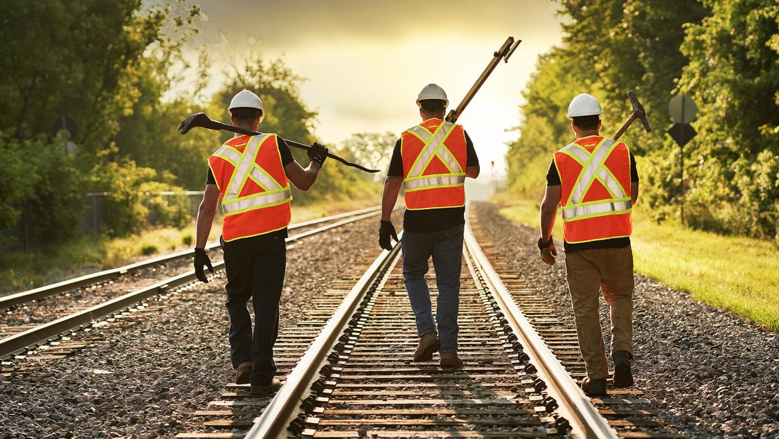 Three Rail Workers walking on the rail tracks with equipment 