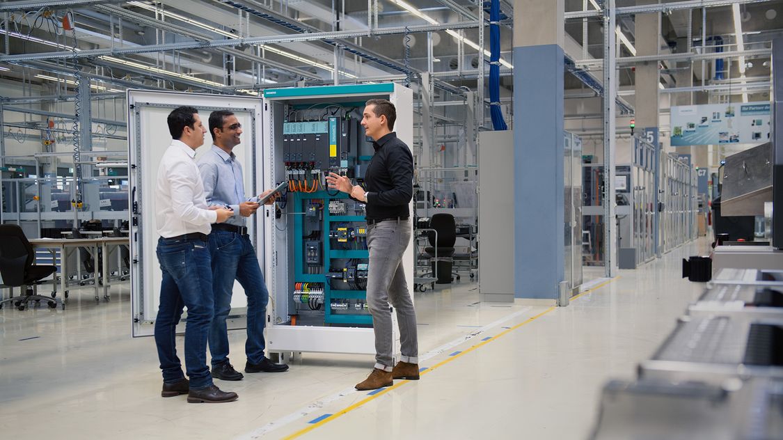 Three men talking in front of a control panel.