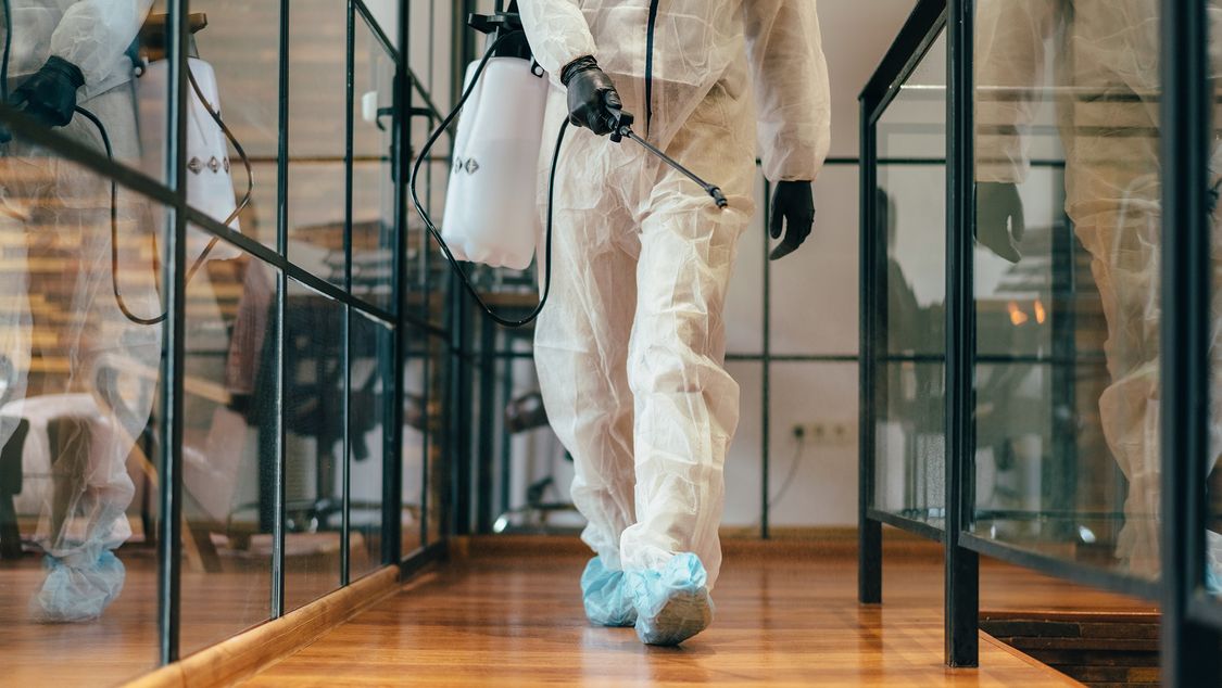 Man in protective suit is decontaminating an office floor.