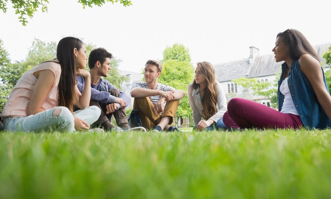 group of college students sitting in the grass on campus