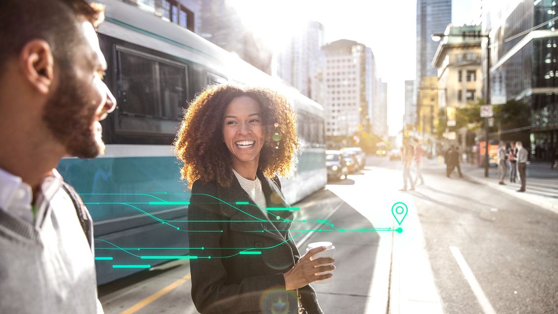 Two smiling people cross a street in a bright, vibrant city with a tram behind them; digital elements over the image display the possibilities offered by smart city solutions for urban transport.