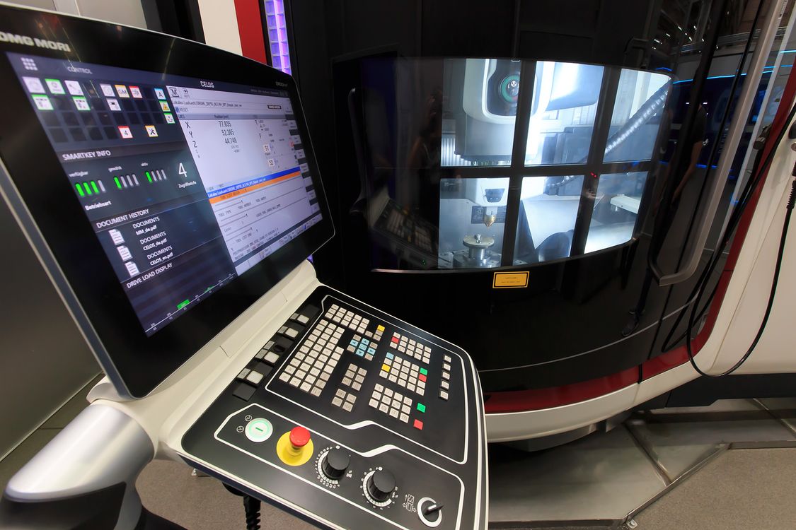 Foto der Bedeintafel einer DMG-Mori-Maschine mit SINUMERIK-CNC, i intergrund die dazugehörige Maschine mit gerüstetem Additive-Manufacturing-Kopf 