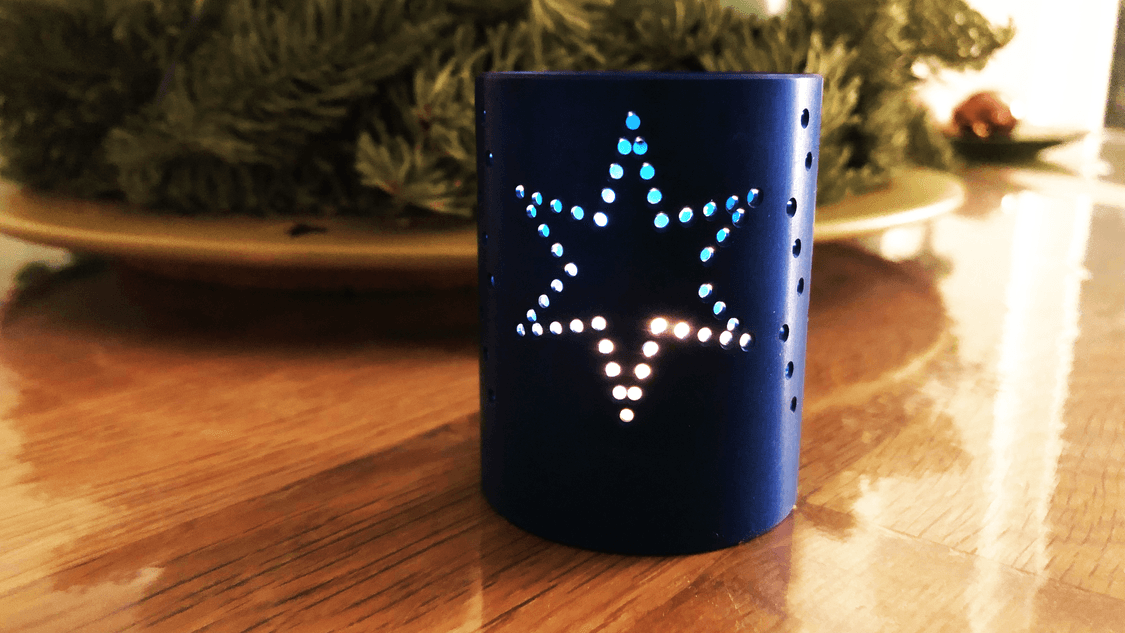 Photo: tealight holder "Star cup 2022", the candle is burning, light pattern on the table. 